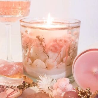 Pink champagne luxury soy gel scented candle stands next to a glass of pink champagne a pink soy wax candle, surrounded by pink and white florals