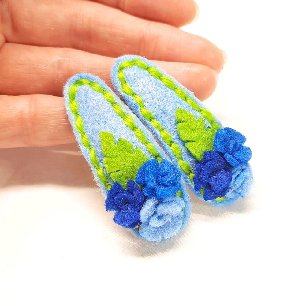Cute hair clips covered in blue felt with matching roses and stitching. Gentle on delicate hair.