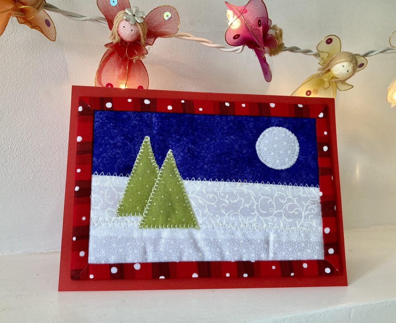 Christmas card in fabric with two trees and moon against a snowy background