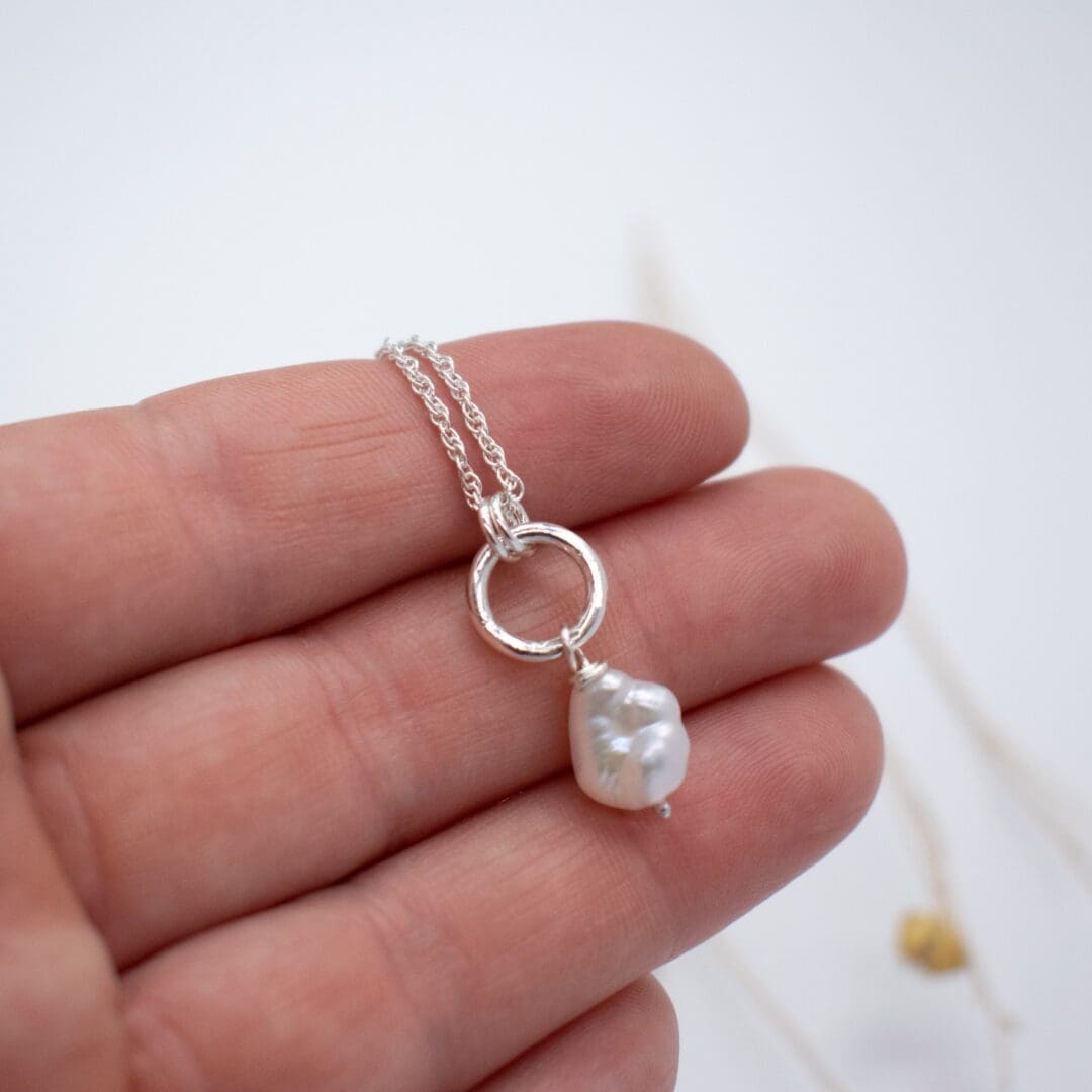 pearl and silver necklace rests on a hand against a white background