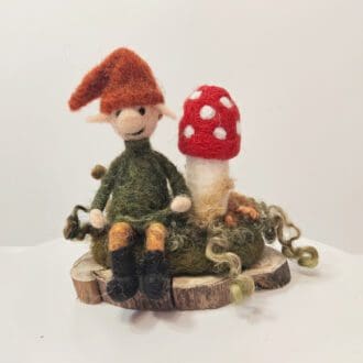 needle felted elf sitting next to a red spotted toadstool