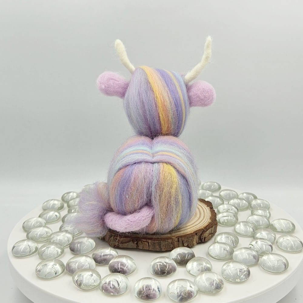 back view of Pastel coloured needle felted highland cow on wood slice.