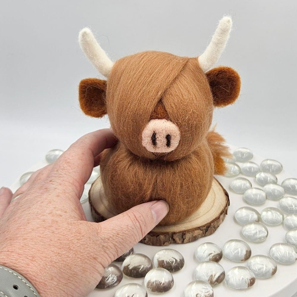 hand holding a needle felted highland cow traditional red