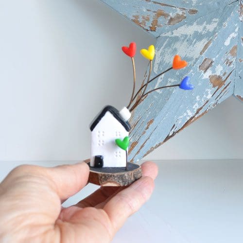 Miniature clay Scandi house set on a log slice with multi-coloured hearts.