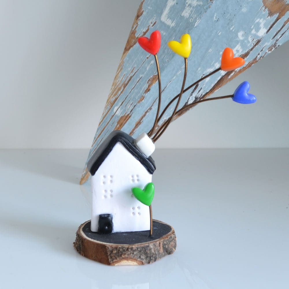 Miniature clay Scandi house set on a log slice with multi-coloured hearts.