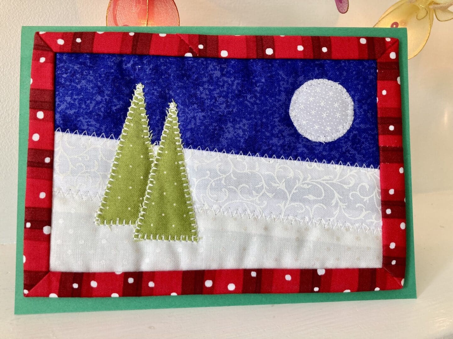 Christmas card in fabric with two green trees and a blue moon against a winter background