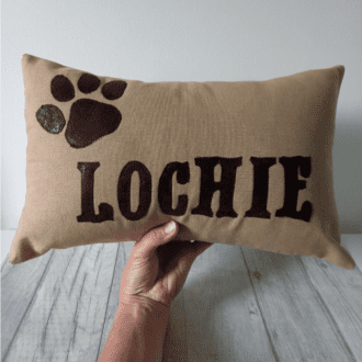 hand holding custom dog cushion with Lochie name and paw motif