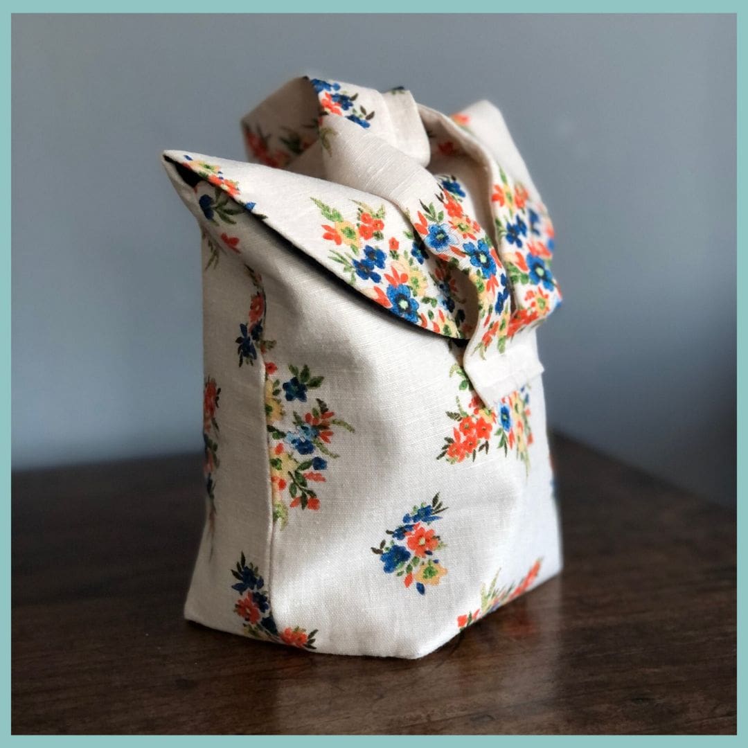 cream floral linen bag sits, side on, on top of wooden table
