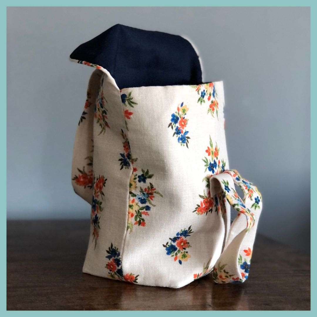 cream floral linen bag, open, sits on top of wooden table