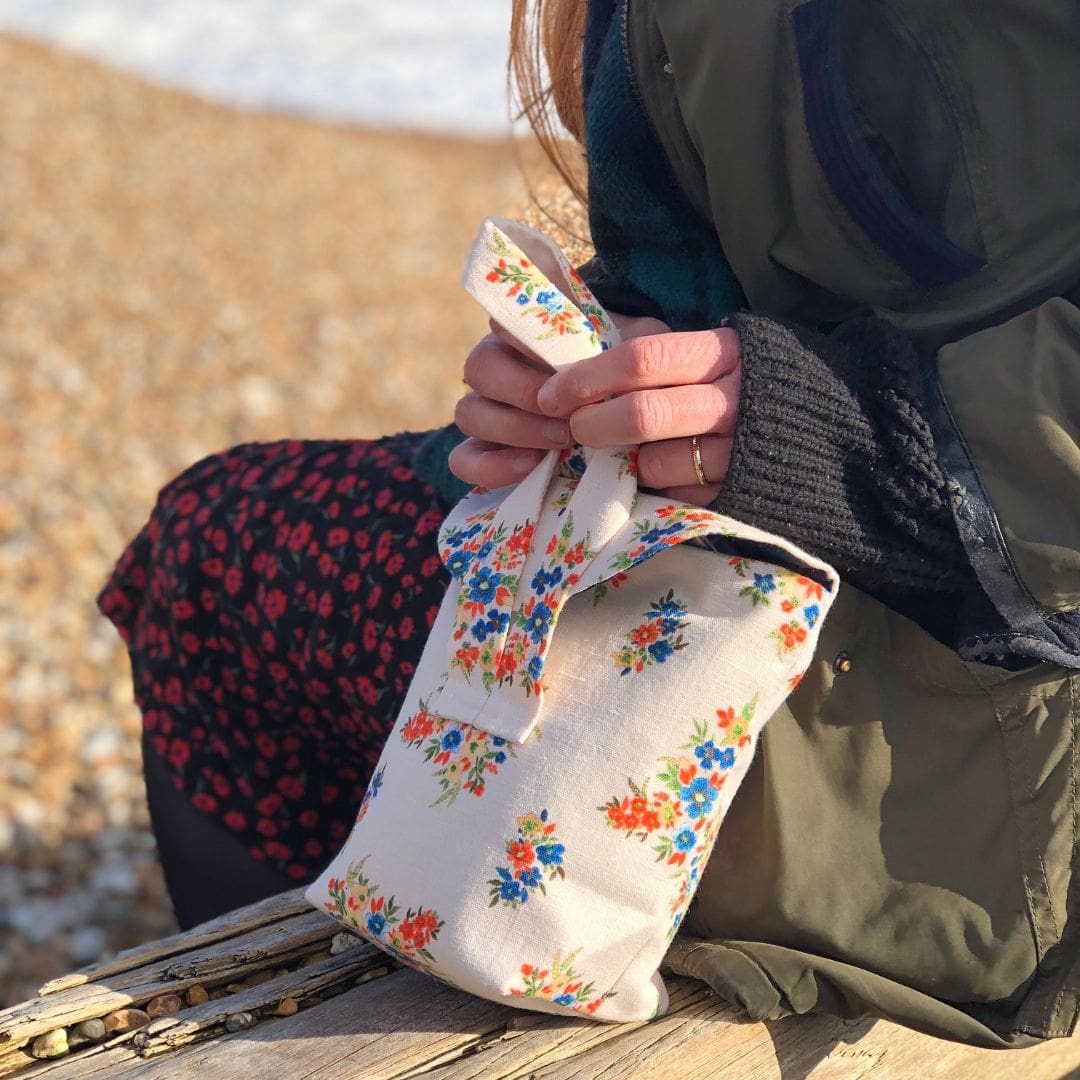 cream floral linen bag sits next to a girl in a green coat sitting on the beach