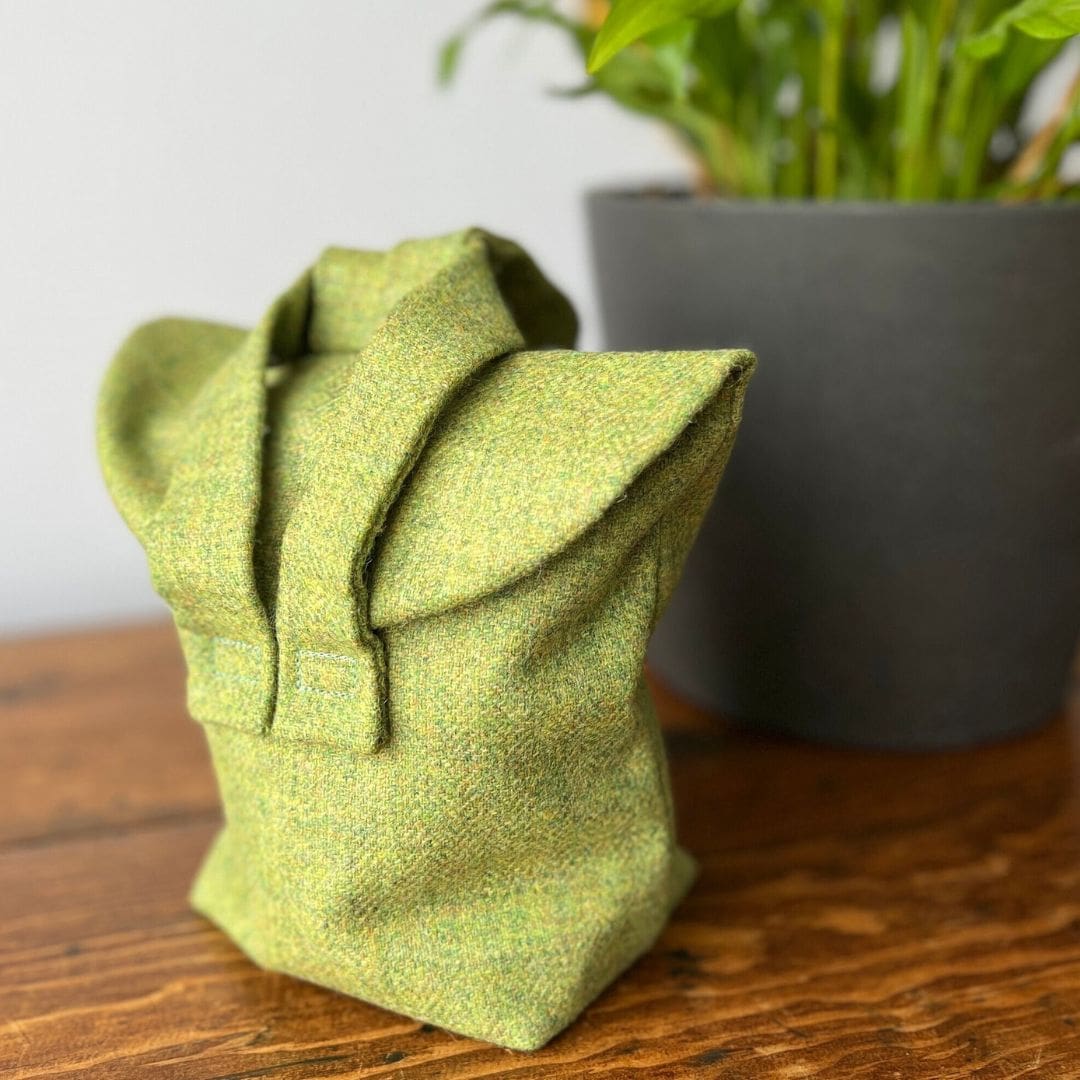 small green 1940s style bag sitting on a wooden table in front of a grey pot with a plant in