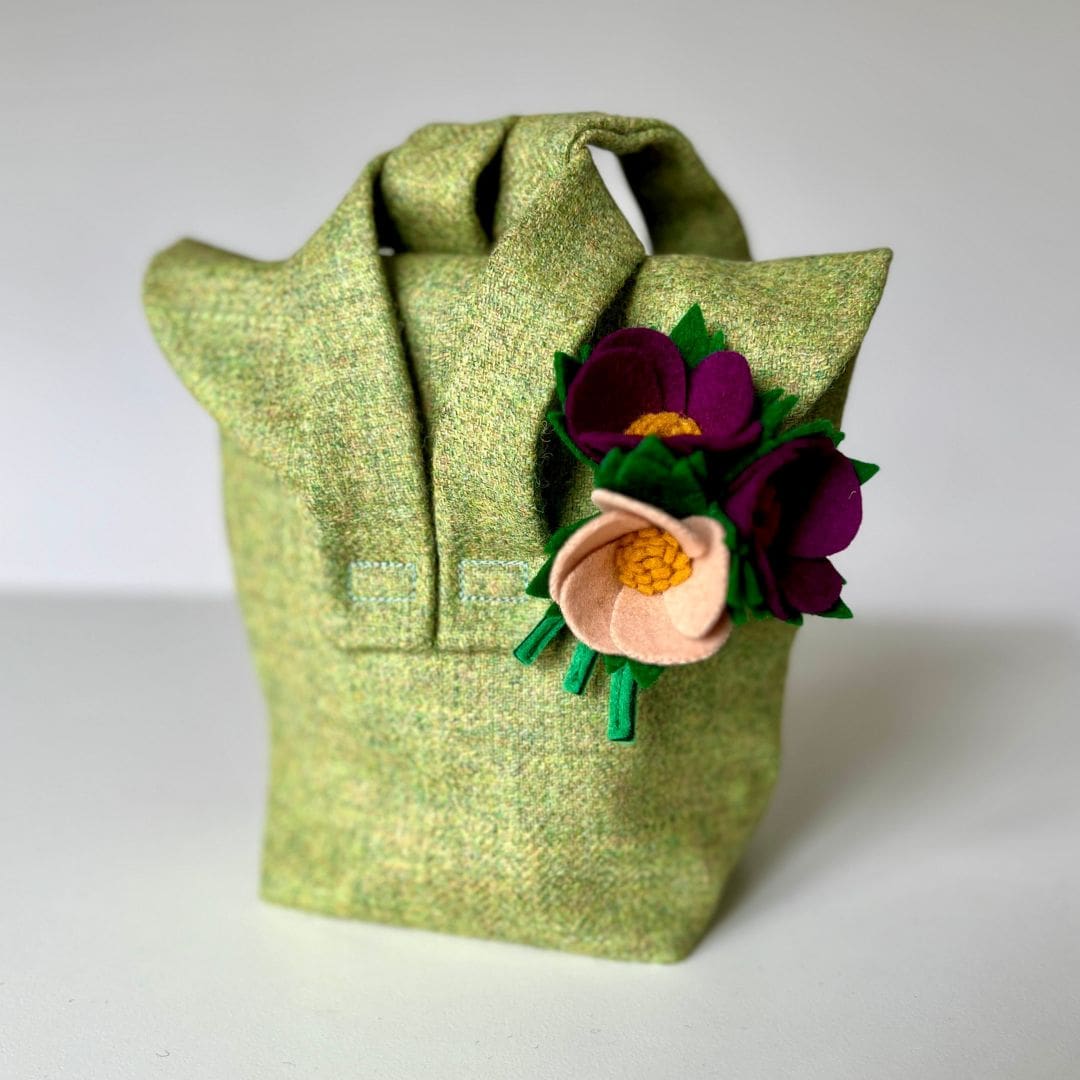 small green cloth bag with a flower brooch attached on a white background