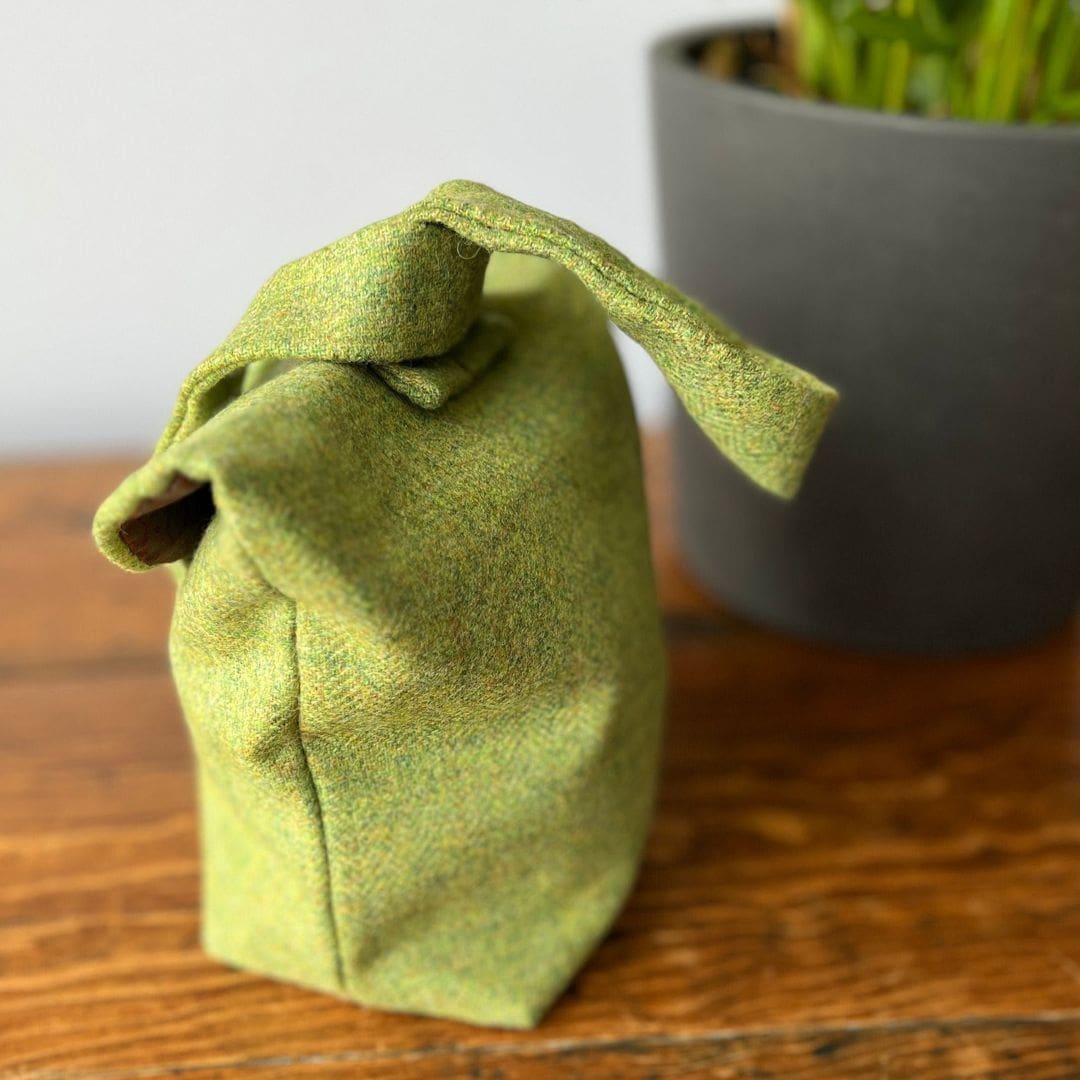 back view of a small bag made of green wooden cloth sitting on a wooden table in front of a plant pot