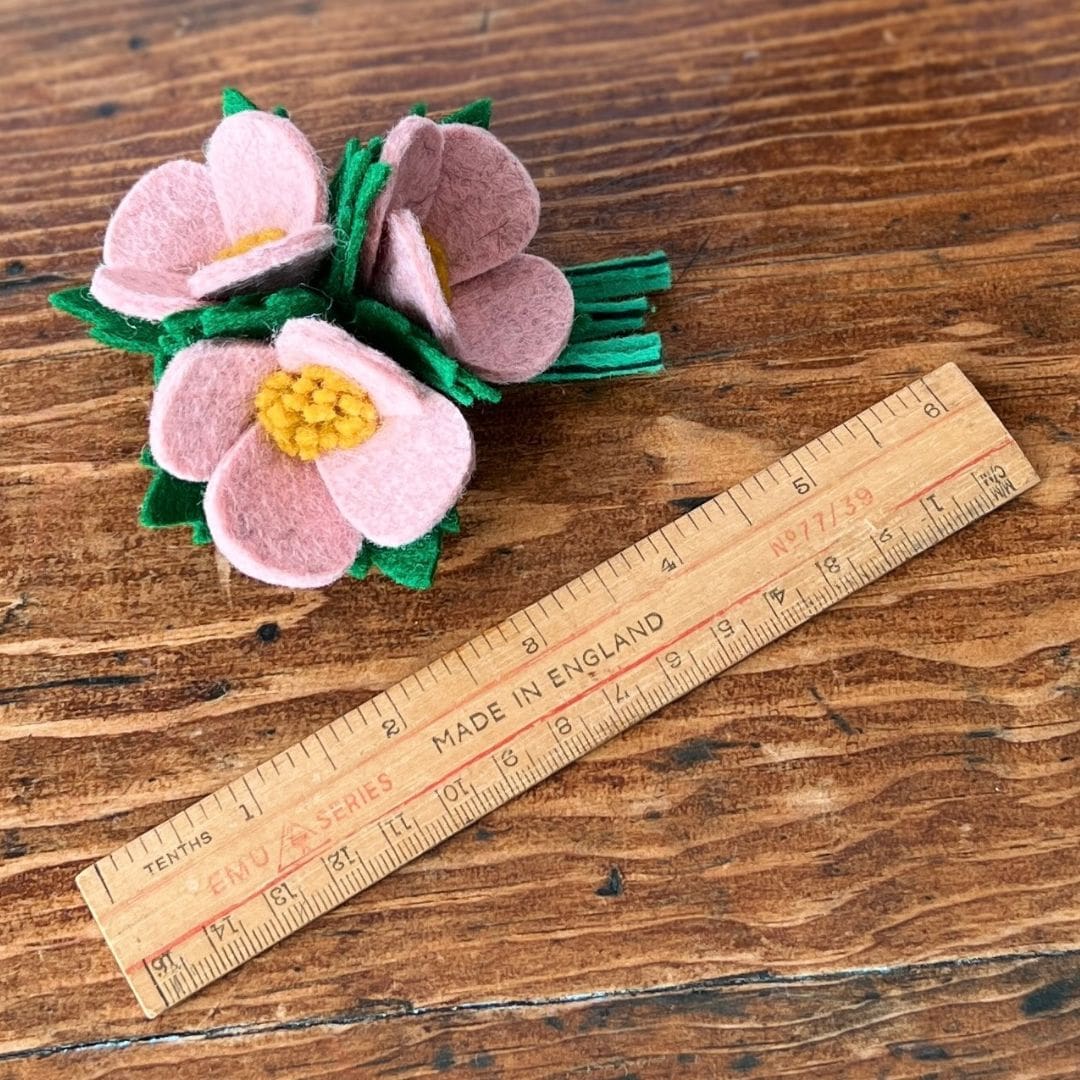 pink corsage brooch next to a vintage style wooden ruler to show the scale of the brooch