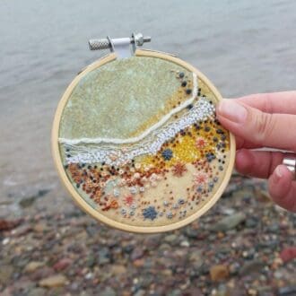 Hand embroidered close up of the shoreline at a pebbly beach 4 inch embroidery hoop.