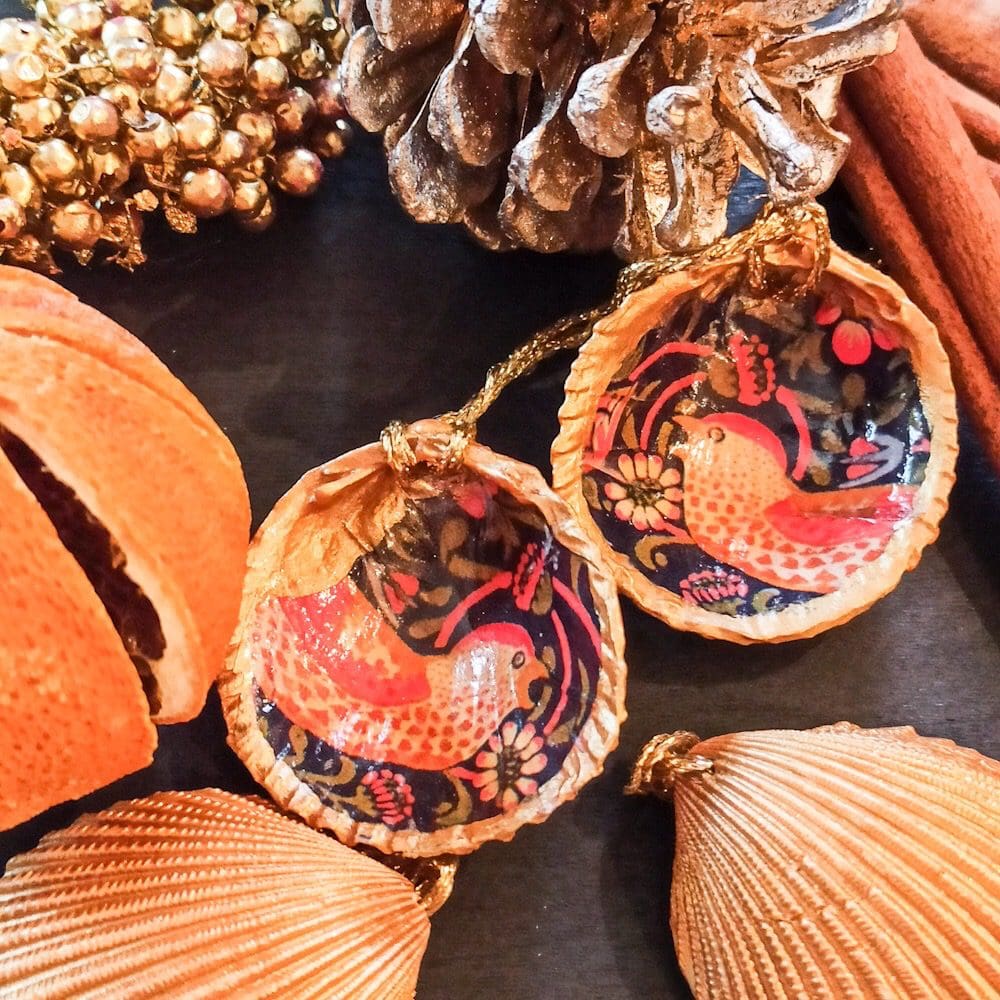 A pair of William Morris gilded decoupaged large cockle shell Christmas decorations are surrounded by dried oranges, cinnamon sticks and festive gold berries