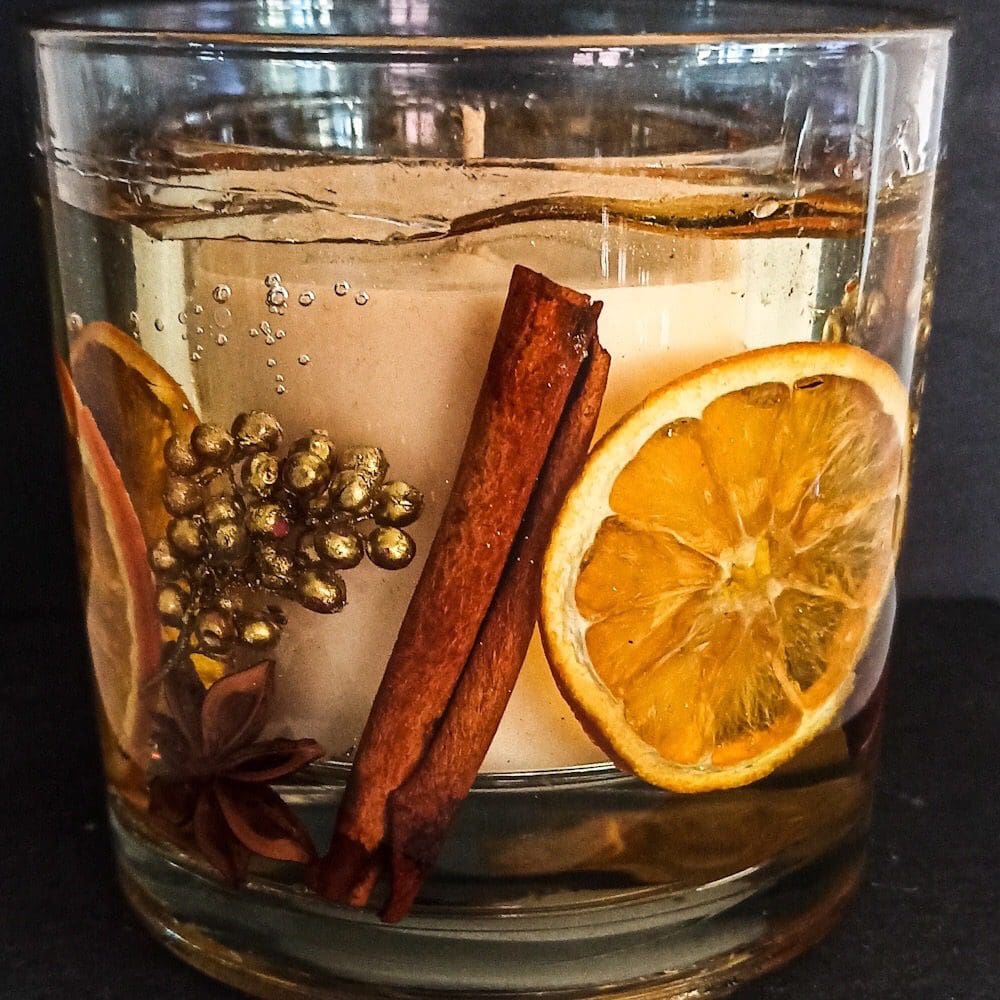 Orange spice large soy and gel wax luxury statement candle decorated with real orange slices, cinnamon sticks, gold berries, star anise and crushed gold crystal is set against a dark background