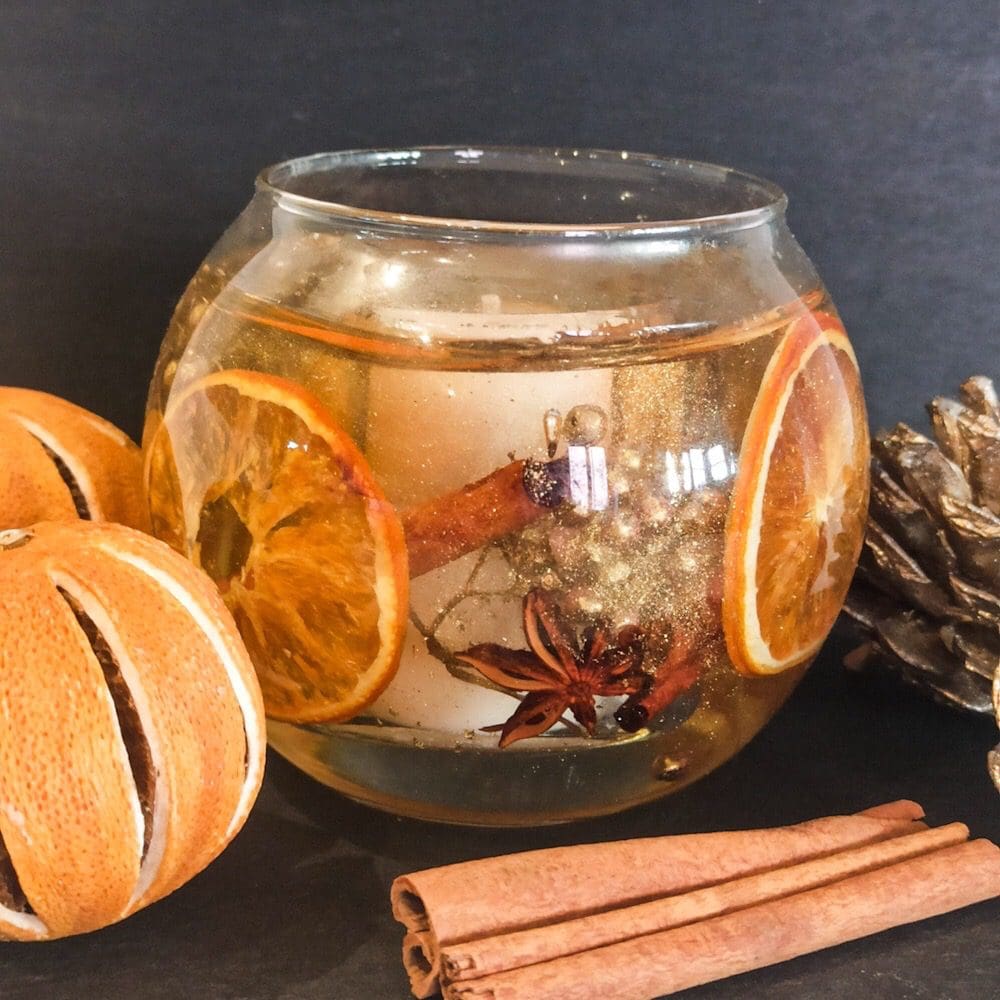 Christmas Orange Spice soy and gel wax candle with whole slices of dried orange, gold berries, cinnamon sticks and star anise on a dark slate background surrounded by dried oranges, cinnamon sticks and fir cones.