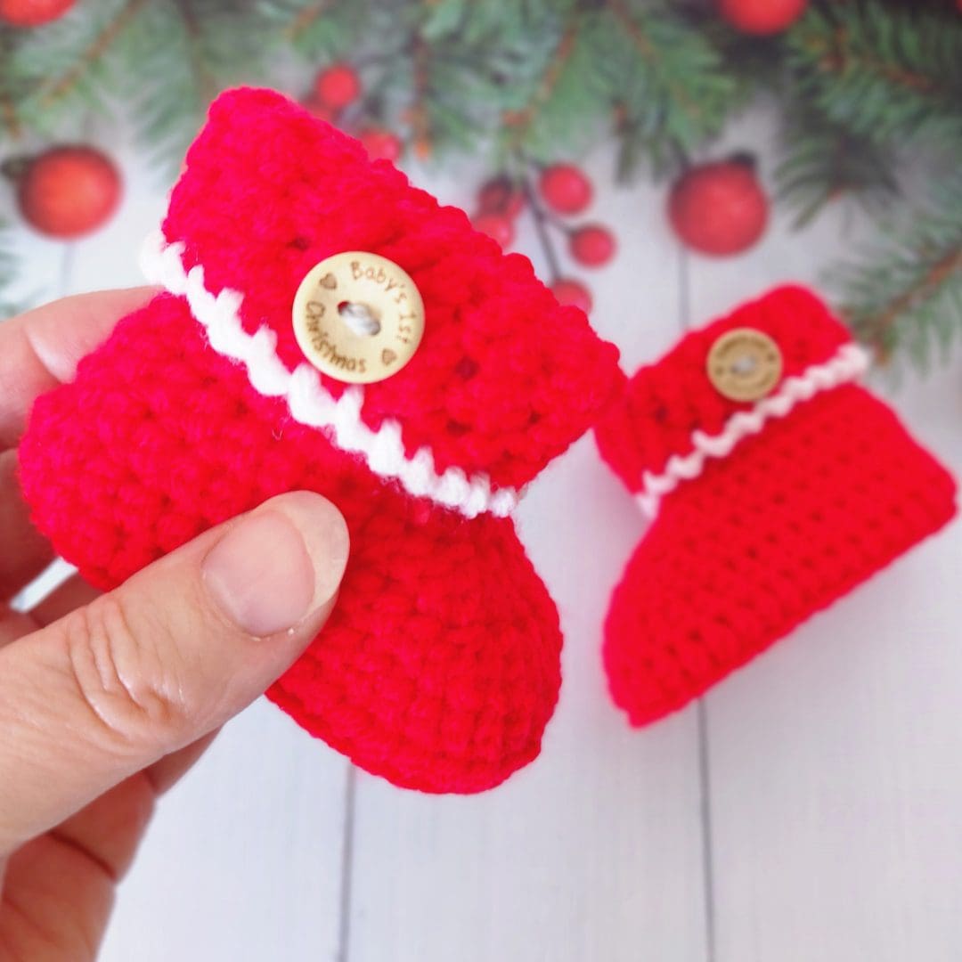 Christmas themed baby booties, made in red with a white edge added to the textured cuff. an Ultrasuede tag is added to the cuff saying santas little helper