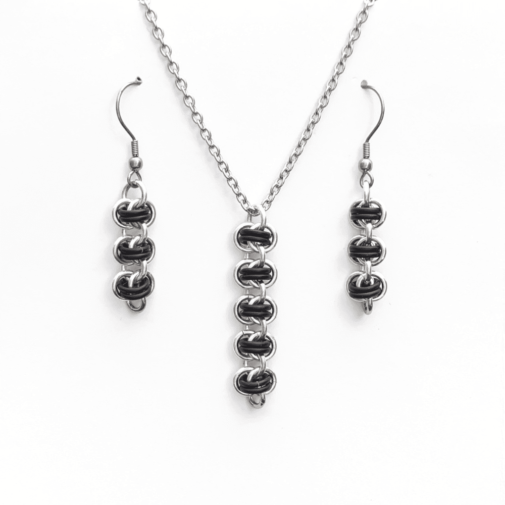 a matching necklace and earring set. The pendant and earrings have been made using silver and matt black coloured rings woven into the chainmaille barrel weave pattern.
