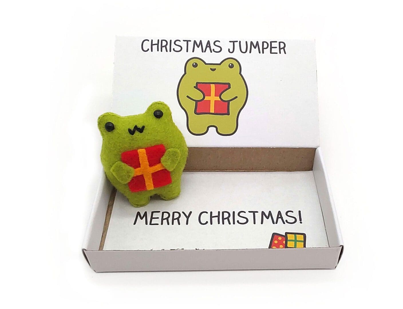 Cute handmade frog Christmas gift. A happy felt frog holding a Christmas presentin an illustrated matchbox that reads Christmas Jumper on the outside and Merry Christmas on the inside.
