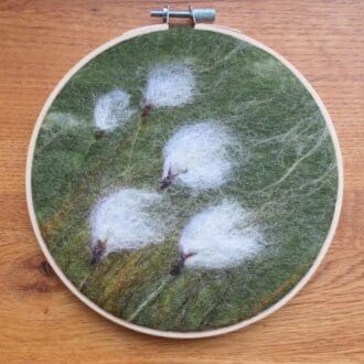 A wool felt picture of moorland cotton grass in a bamboo hoop.