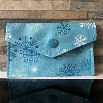 Fabric gift card holder with blue and white snowflakes on a blue cotton and lined with darker blue cotton. Closing with a mid-blue snap popper.