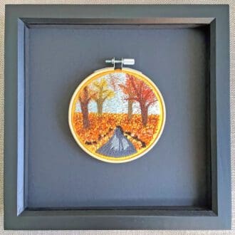 framed embroidered picture reflecting an autumn wooded landscape