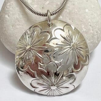 A large silver domed circle necklace embossed with flower print