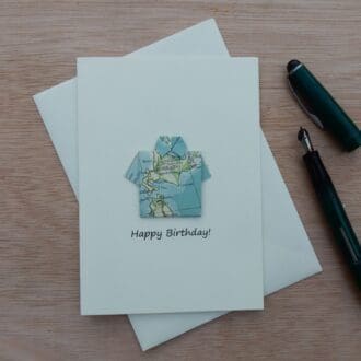 Happy Birthday lying flat on envelope with fountain pen next to it. Card shows an origami shirt shape made using an atlas page
