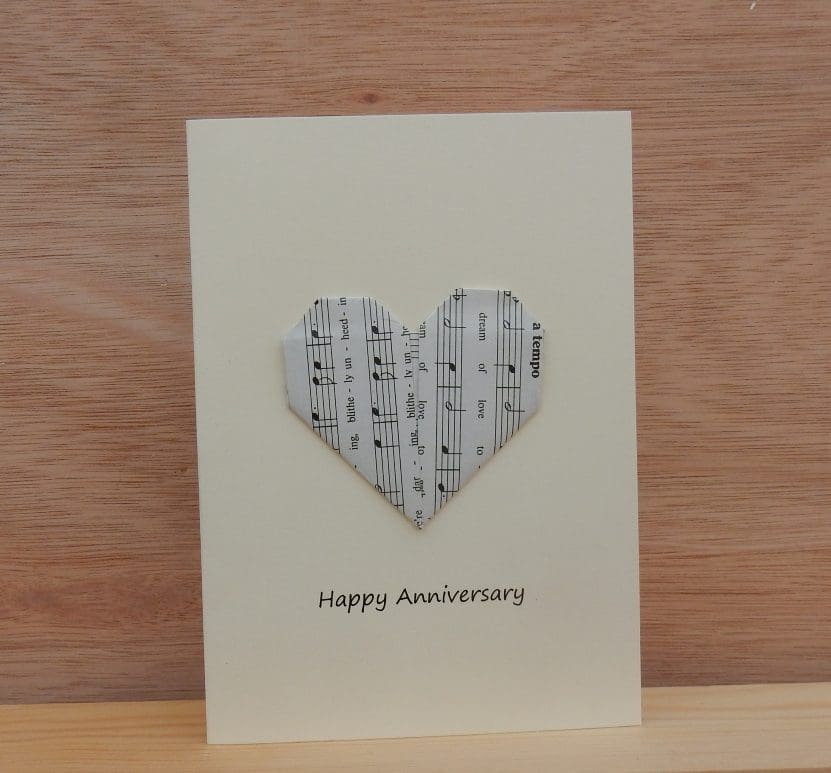 Standing cream coloured Happy Anniversary card. Shows origami folded sheet music heart.