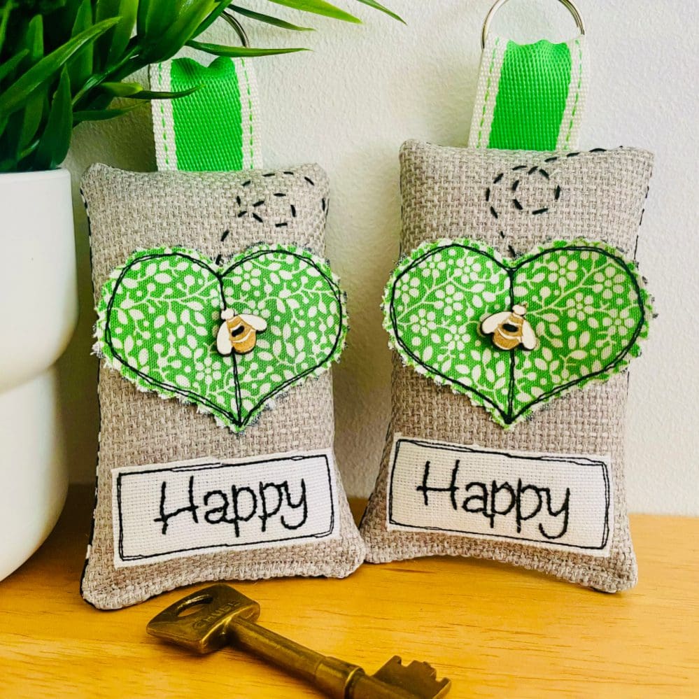 Green fabric heart keyring with wooden bee detail and embroidered text saying Happy