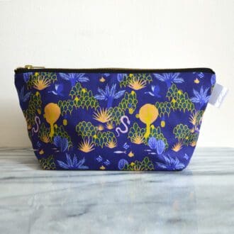 In the centre of the image is a bright blue cotton make up bag with a hand painted jungle print and finished with a brass zip across the top.