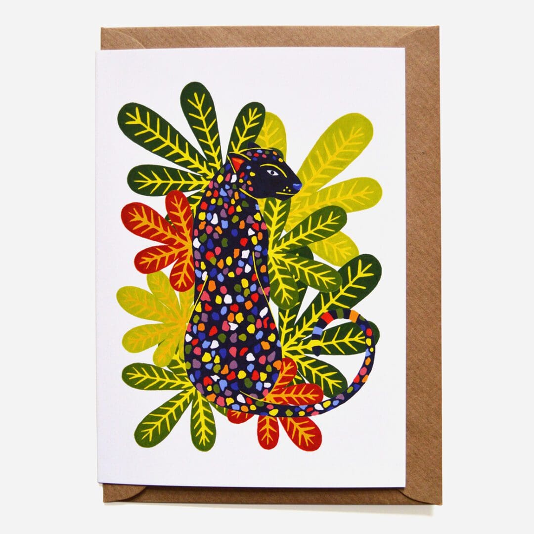 An A6 greeting card with brown envelope. In the centre of the card is a black leopard with rainbow coloured spots. Surrounding the leopard are green, red and yellow foliage.