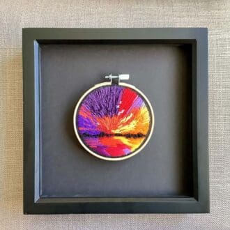 framed hand embroidered scene of a reflecting sun setting over water