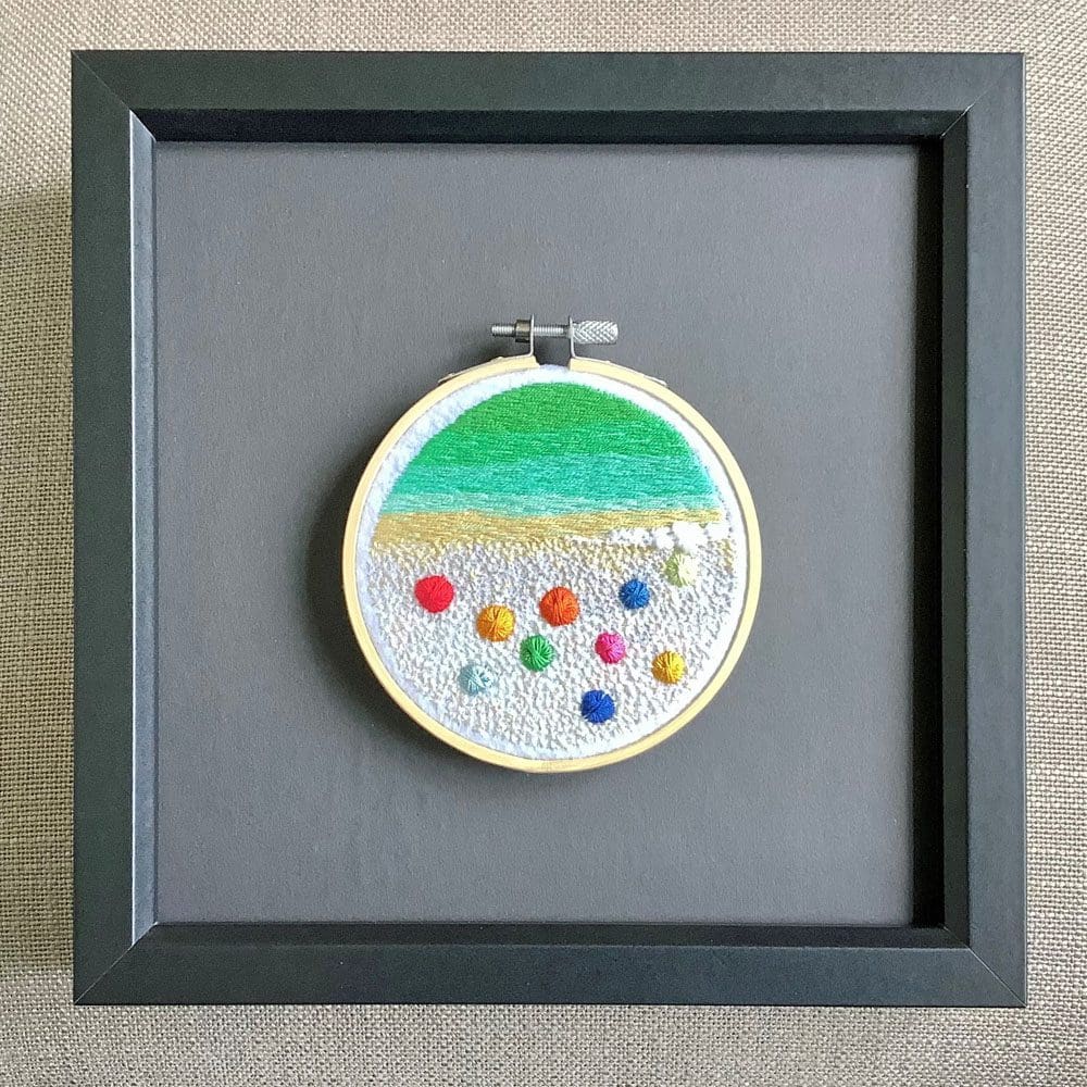 framed embroidered picture showing an aerial impression of a sandy beach dotted with sun parasols