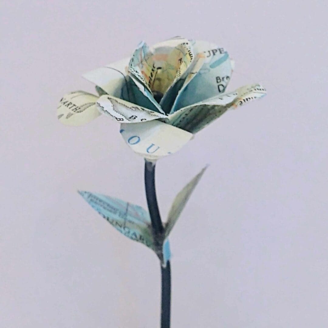 Miniature-paper-rose-decoration-made-from-a-map-set-on-a-wire=stem-in-a-wooden-cotton-reel