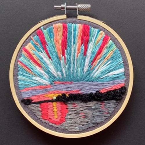 a hand embroidered scene of the sun rising over water