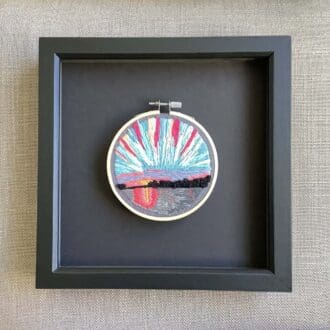 framed hand embroidered scene of the sun rising over water