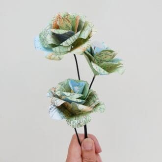Three folded map paper roses on wire stems shown held in a hand