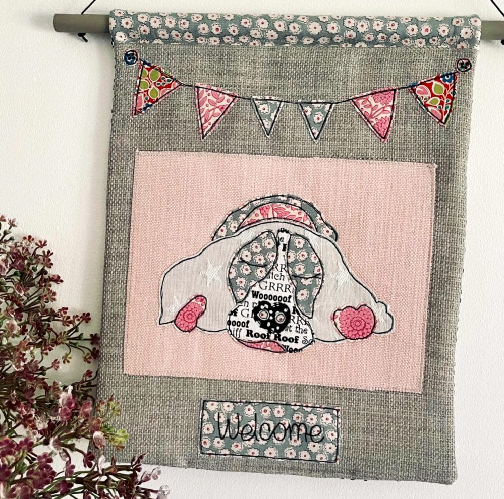 Pink textile appliqué sleeping spaniel decorative wall hanging with bunting and welcome text