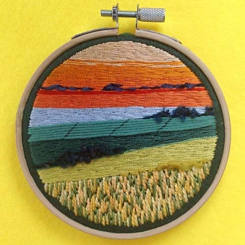embroidered scene of the setting sun over fields