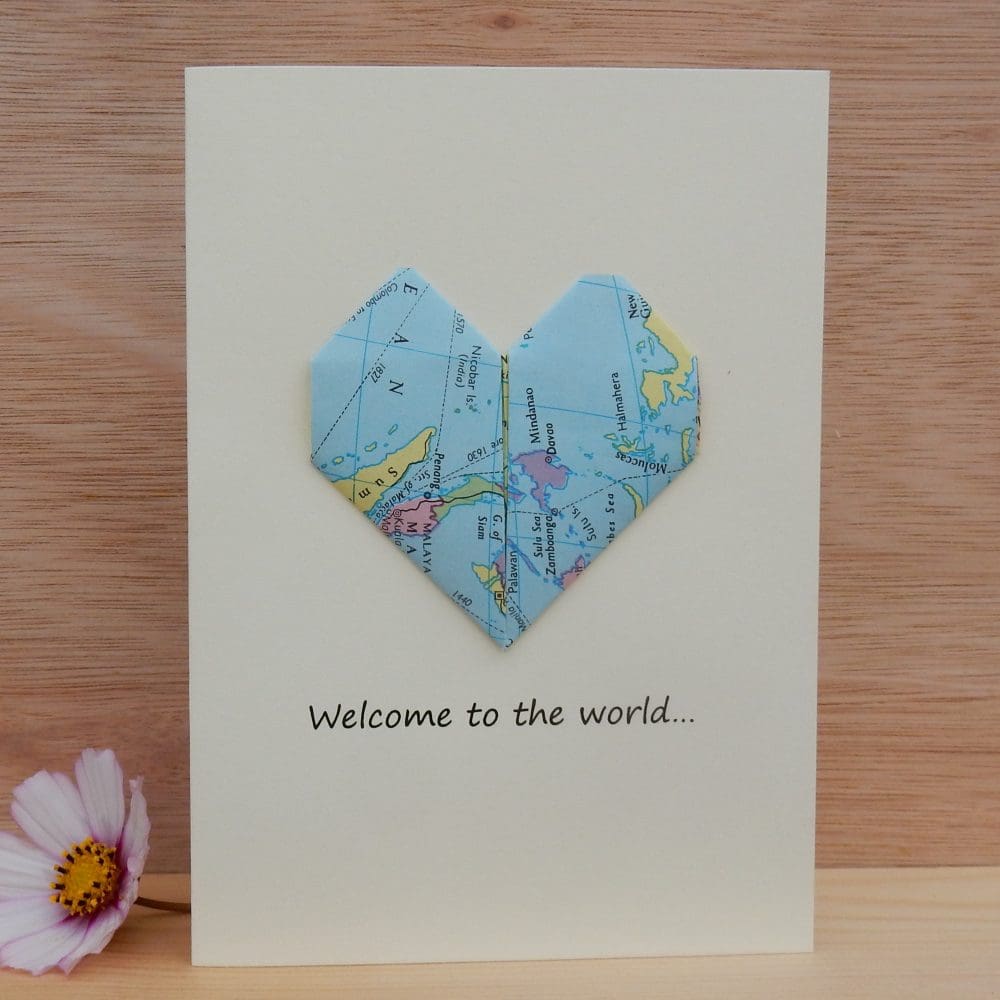 New baby card standing next to a flower. Shows an origami map heart on the card.