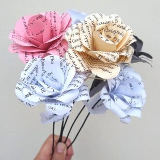 hand holding bunch of five multicoloured paper roses made using upcycled stationery