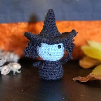Crochet Witch mini figure for Halloween. She has a duck blue face, floppy pointy hat and mad looking hair though she is smiling!