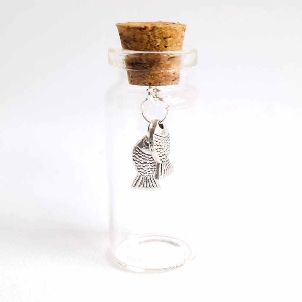 two small silver fish charms hanging inside a miniature glass bottle, designed by undet the blossom tree