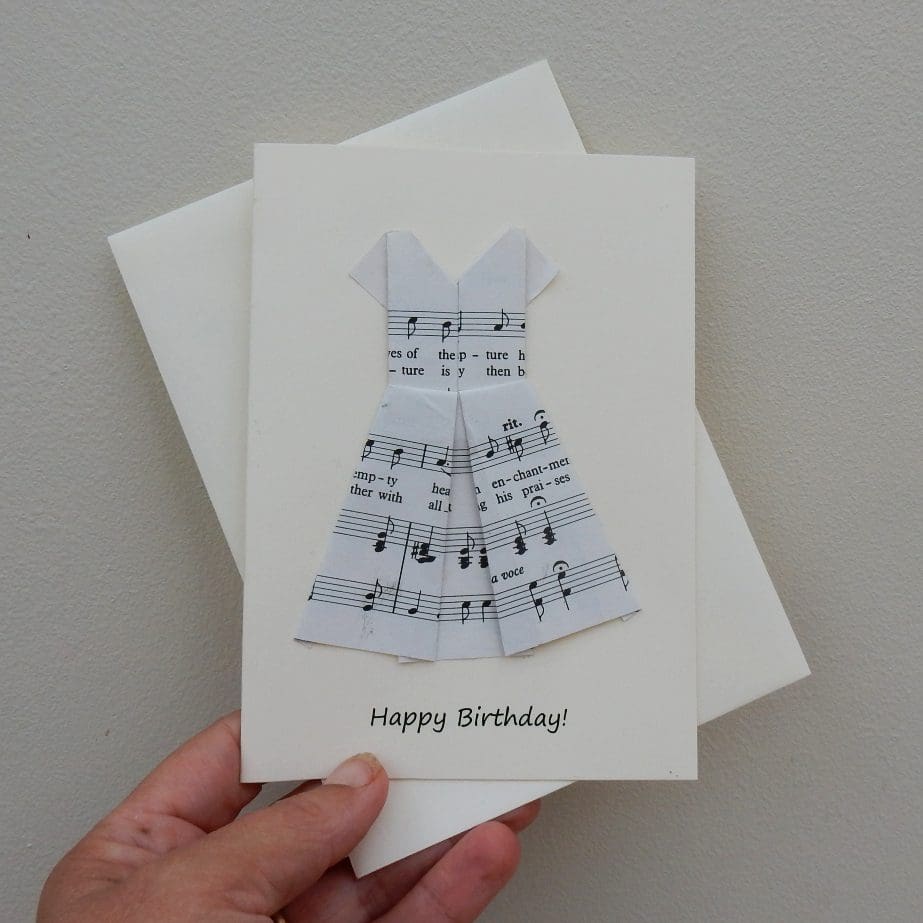 Hand holding Happy Birthday card showing origami folded dress made using sheet music. Writing says Happy Birthday