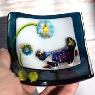 dark blue glass trinket dish with a multicoloured dichroic cat in a meadow scene
