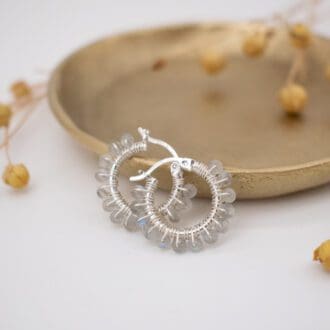 gemstone beaded hoop earrings resting on brass dish with dried flowers