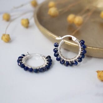 lapis lazuli earrings resting on small brass dish on white background with dried flower stems